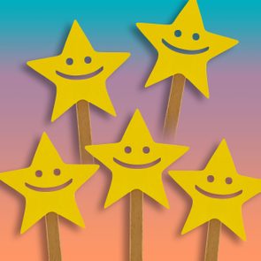 Yellow star cutouts with happy faces mounted on sticks, set against a gradient background of blue, pink, and peach.