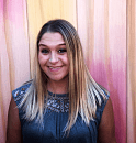 A person smiles while standing in front of a backdrop with vertical pink and beige stripes.