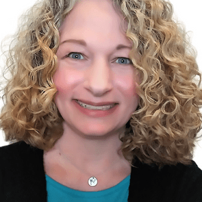 A person smiles warmly, wearing a turquoise top and a round pendant necklace, framed by curly blonde hair, with a plain white background.
