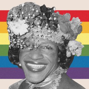 Person smiling, wearing a floral headpiece, against a rainbow-striped background.