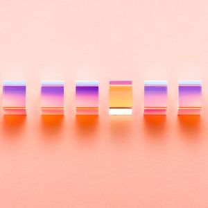 Colorful transparent blocks reflect light, aligned in a row against a soft peach background.