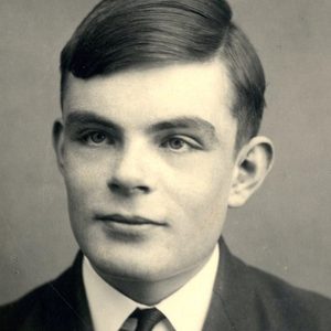 Young man gazes forward, expression calm, wearing a suit and tie, against a plain background.