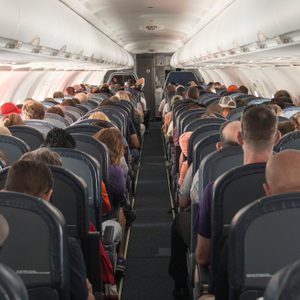 Passengers sitting quietly on seats inside a narrow airplane cabin, with overhead bins closed, during a flight.