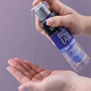 Bottle dispenses clear serum into a palm, against a plain purple background. Text on the bottle reads 