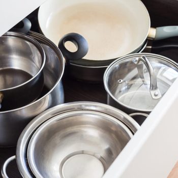 Pots and pans arranged in an open kitchen drawer on a wooden floor, showcasing various sizes and materials, including stainless steel and nonstick coatings.