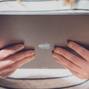 Hands holding a tablet with an Apple logo; person wearing a striped shirt in the background.