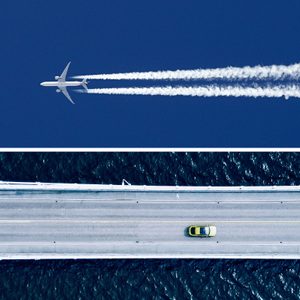 Airplane flies high releasing contrails in a clear blue sky; below, a yellow car drives on a bridge over dark water.