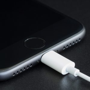 A smartphone charges on a black surface with a white cable connected to its bottom port.