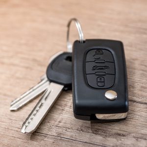 Car keys with a remote lie on a wooden table, showing buttons for lock, unlock, and other functions.