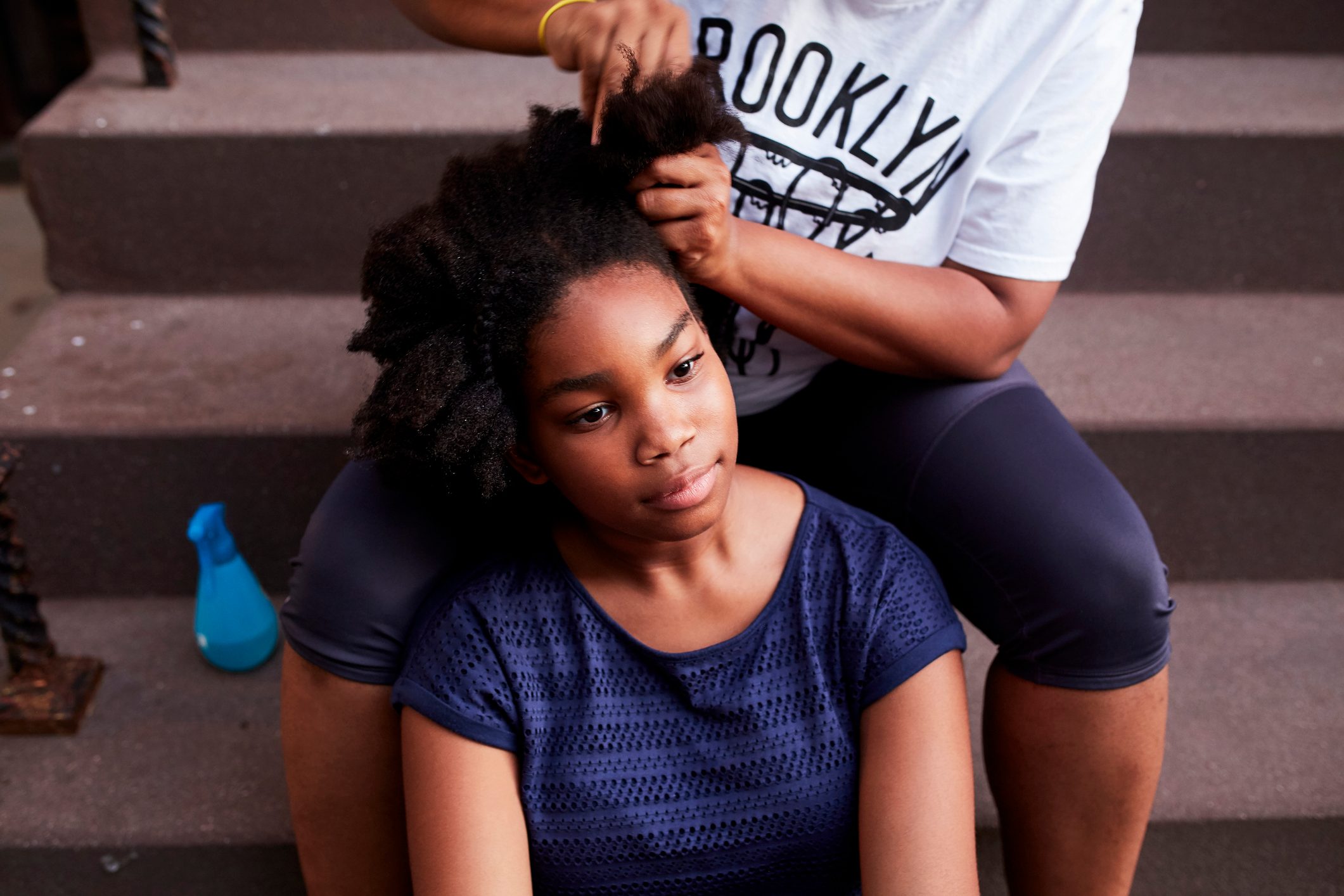 Black mother styling hair of daughter on staircase