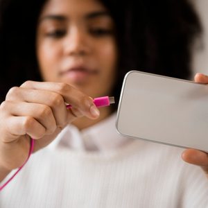 Person connects pink cable to phone, holding it in hand, indoors.
