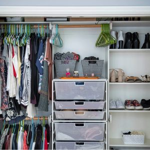 Clothes hang neatly in a closet; storage drawers and shelves hold shoes and baskets, organized within a tidy, open wardrobe.
