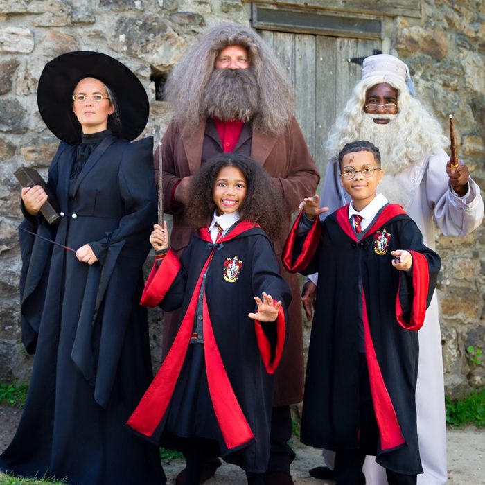 Five people posing in wizard costumes in front of a stone wall, holding wands, dressed in academic robes, and smiling.