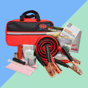 Jumper cables and emergency supplies spread on a surface, near a red and black bag, with pamphlets, flashlight, and first-aid items.