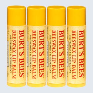 Four yellow lip balm tubes stand aligned, labeled with red text detailing ingredients like vitamin E and peppermint, indicating a natural formula.