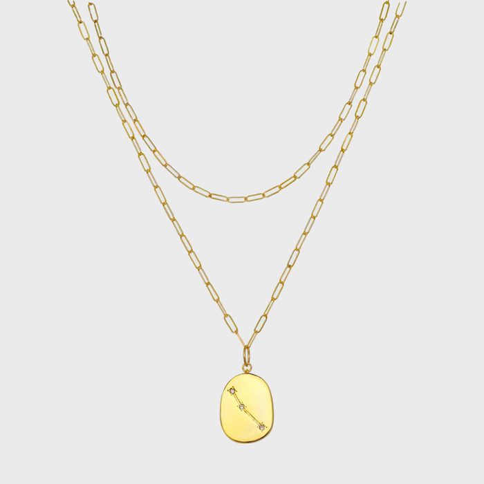 Two gold chain necklaces, one with a plain oval pendant featuring small stones in a line, suspended against a plain white background.