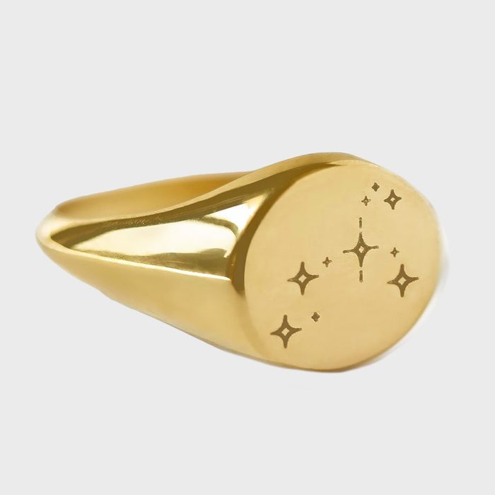 A gold ring with star engravings sits on a neutral background.