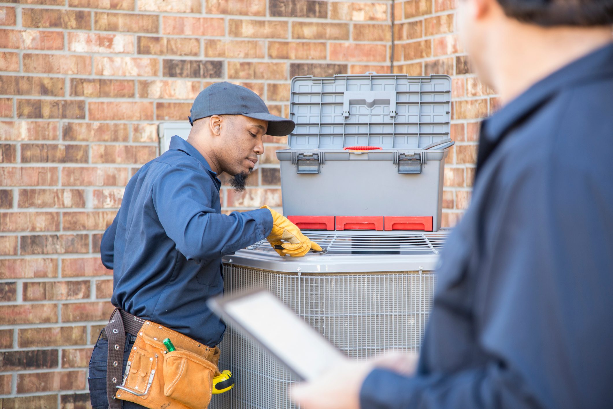 Multi-ethnic team of blue collar air conditioner repairmen at work.