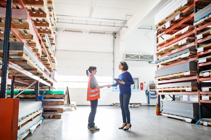 Businesswoman shaking hands with worker in large warehouse. Manager and worker handshake in storehouse