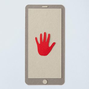 A red paper hand resting on a cardboard smartphone cutout, placed on a light surface.