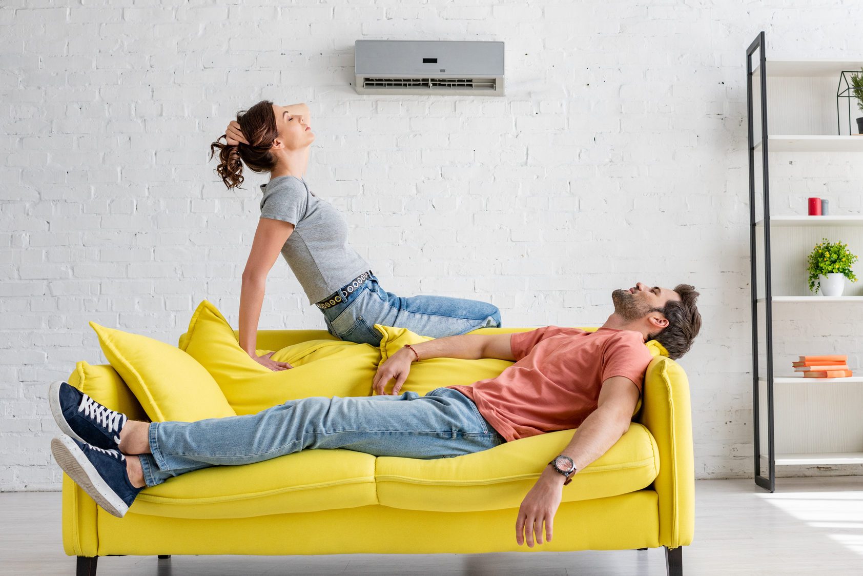young man and woman resting on yellow sofa under air conditioner at home