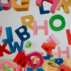 Colorful wooden letters fall against a plain background, scattering chaotically, creating a playful and dynamic scene.