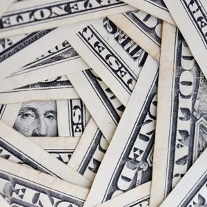 Dollar bills layer concentrically, revealing a partial face through the gaps. The scene forms a spiral pattern with visible currency details.