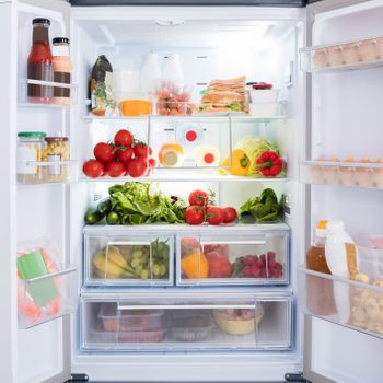 Refrigerator displaying neatly arranged fruits, vegetables, drinks, eggs, and condiments in a well-lit kitchen setting.