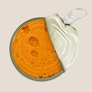 An opened can sits with bright orange contents visible, surrounded by a pale background.