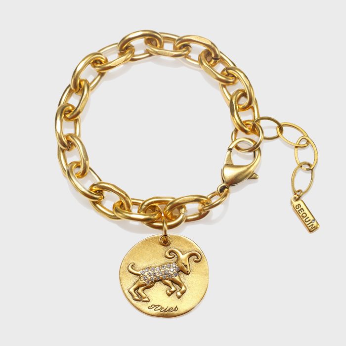 A gold chain bracelet displays a round Aries charm with a sparkling ram. The tag reads 