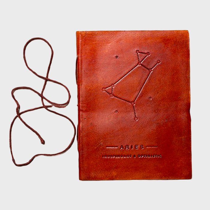 Brown leather notebook displays Aries constellation, lies next to a twisted cord, against a plain background. Text reads 