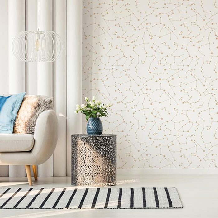 A white lamp hangs over a patterned side table with flowers, next to a cozy sofa in a stylish, softly-lit room.