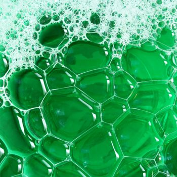 Bubbles cluster, forming intricate patterns in bright green liquid, creating a textured, layered effect.