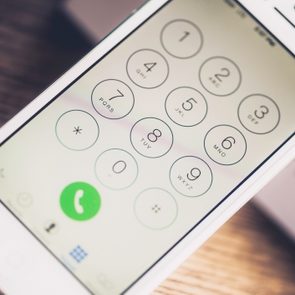 Smartphone displays a dial pad with numbers and letters, featuring a green call button, placed on a wooden surface.