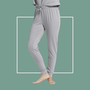 Gray sweatpants hang loosely on a person standing barefoot against a solid green background with a white square outline.