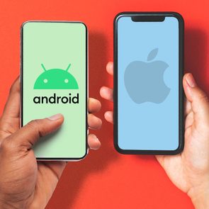 Two hands hold smartphones, displaying Android and Apple logos on green and blue screens against an orange background.