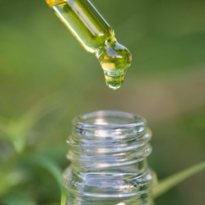 Dropper releases green liquid into a clear glass bottle, set against a blurred green background.
