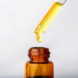 A glass dropper releases yellow liquid into an amber bottle against a plain, light background.