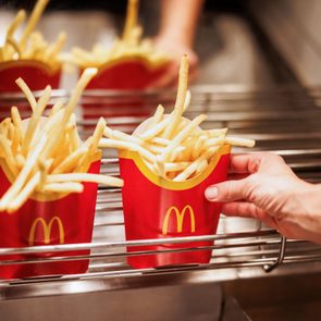 French fries sit in red containers on a metal rack, with a hand grabbing one.