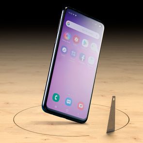Smartphone descends through a wooden surface, displaying apps and browser, next to a saw protruding upwards.