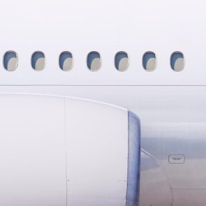 Airplane exterior features visible windows and engine, set against a clear sky, highlighting its sleek design and structure.