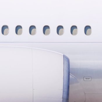 Airplane exterior features visible windows and engine, set against a clear sky, highlighting its sleek design and structure.