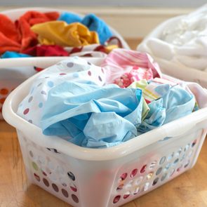 Laundry baskets hold sorted clothes with varied colors and patterns on a wooden floor, suggesting a household chore setup.