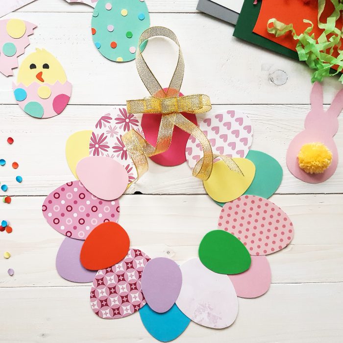 The child makes crafts with his own hands for the Easter. Colorful handmade from multi-colored paper. Scissors, cardboard, eggs, chicken, rabbit. Art creativity on a wooden table. Top view, copy space