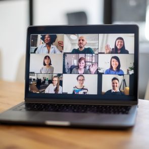 Laptop displays a video call with nine people interacting in a modern, well-lit room.