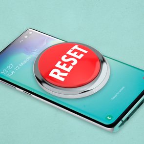 A large red reset button sits on a smartphone screen displaying the date and time, surrounded by a light teal background.