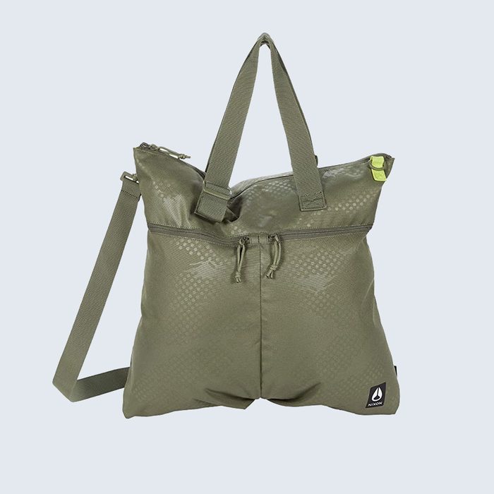 Green tote bag resting upright, featuring two handles, a detachable strap, and a small triangular logo; placed against a light blue background.