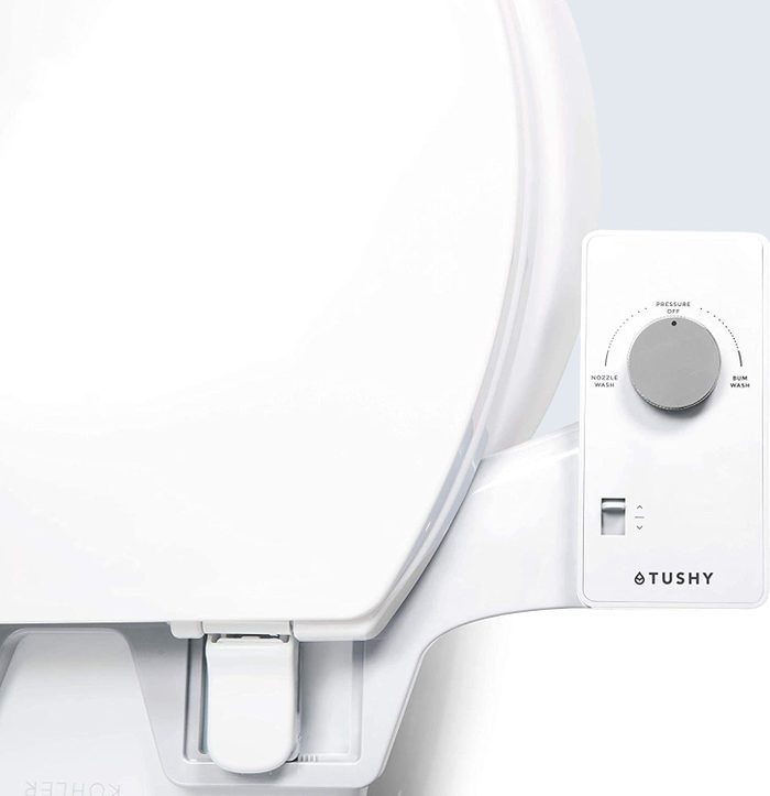 Bidet attachment, featuring control dial, is mounted on white toilet seat lid. Text shows 