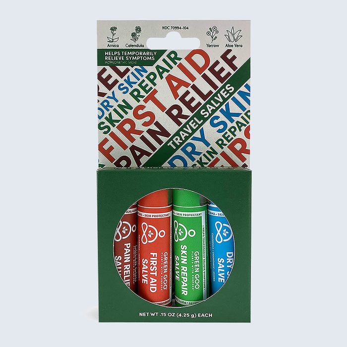 Three salve tubes stand in packaging, labeled for first aid, skin repair, and dry skin relief, surrounded by natural ingredient illustrations and text.