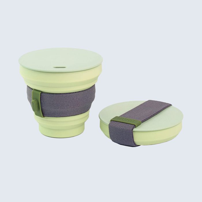 Collapsible green silicon cup stands open, band wrapped. Another lies folded beside it. Simple, minimalistic design on light blue background.